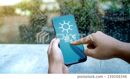 Close up of hands using a mobile weather app showing a sunny forecast while it is raining outside. Concept of digital technology, meteorology, and climate prediction Close up of hands using a mobile weather app showing a sunny forecast while it is raining outside. Concept of digital technology, meteorology, and climate prediction 139208346