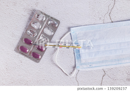 A thermometer, a medical mask, and a blister pack of pills on the table top view 139209237