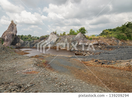 The Ancient Echoes of Nong Bua. Beneath a heavy, silver-fringed sky, a towering shard of rusted stone rises like a jagged spire, keeping watch over a deep, mineral-stained basin. This dramatic terrain The Ancient Echoes of Nong Bua. Beneath a heavy, silver-fringed sky, a towering shard of rusted stone rises like a jagged spire, keeping watch over a deep, mineral-stained basin. This dramatic terrain 139209294
