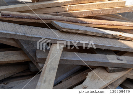 Pieces of wood are piled on each other in a workspace with some sunlight shining on them. This shows various lengths and types of wood Pieces of wood are piled on each other in a workspace with some sunlight shining on them. This shows various lengths and types of wood 139209479