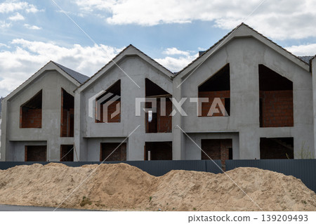 Workers continue the construction of new residential buildings at a site with sand piles in the foreground under a cloudy sky Workers continue the construction of new residential buildings at a site with sand piles in the foreground under a cloudy sky 139209493