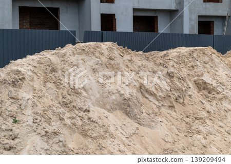 Workers are preparing sand at a construction site with incomplete buildings around. The scene shows raw materials and site barriers 139209494