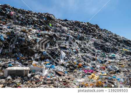 Large pile of trash sits under blue sky, showing various types of waste including plastics, papers, and other items strewn about 139209503