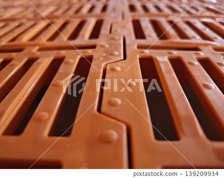 Close up of orange plastic slatted floor panel with perforated slots and interlocking joints used in pig housing systems. Livestock farming, agriculture equipment, animal housing 139209934
