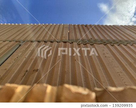 Clay hollow blocks with ribbed surface installed in wall construction under blue sky view from below. Construction, masonry, building materials, architecture, wall building Clay hollow blocks with ribbed surface installed in wall construction under blue sky view from below. Construction, masonry, building materials, architecture, wall building 139209935