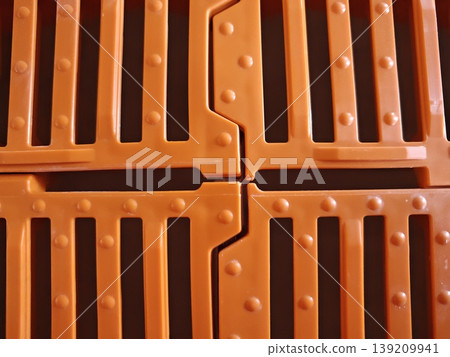Top view of orange plastic slatted flooring panels with interlocking joints and drainage slots for pig housing system. Livestock farming, agriculture equipment, animal housing Top view of orange plastic slatted flooring panels with interlocking joints and drainage slots for pig housing system. Livestock farming, agriculture equipment, animal housing 139209941