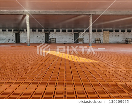 Wide interior of livestock building with orange plastic slatted flooring panels installed across entire floor and concrete columns. Agriculture, pig farming infrastructure 139209955