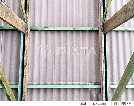 Corrugated roofing sheets mounted on wooden frame with visible support beams in interior construction view. Construction, roofing, building materials, architecture, installation process Corrugated roofing sheets mounted on wooden frame with visible support beams in interior construction view. Construction, roofing, building materials, architecture, installation process 139209979