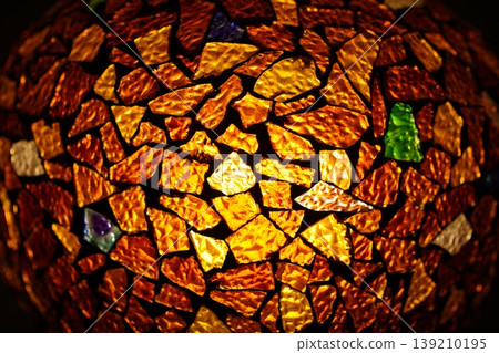 Close-up of colorful mosaic glass texture with warm light, glowing amber and gold stained glass fragments for decorative artistic background. Close-up of colorful mosaic glass texture with warm light, glowing amber and gold stained glass fragments for decorative artistic background. 139210195