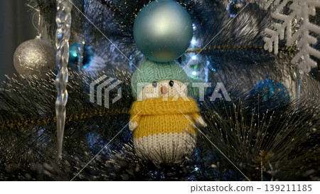 cute knitted penguin balancing shiny blue bauble on head perched on frosted christmas tree branch with icicles and snowflakes whimsical winter decor perfect for holiday greeting cards 139211185