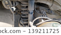 Close up view of cars rear suspension system reveals dusty shock absorber and coil spring. Components show signs of wear, road grime, highlighting the intricate mechanical structure underneath vehicle 139211725