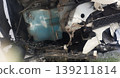 The image shows the internal damage to a vehicle's front end following an accident. Exposed components include a blue washer fluid reservoir, bent metal frames, and shattered plastic bumper parts 139211814