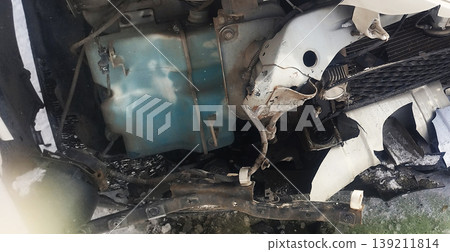 The image shows the internal damage to a vehicle's front end following an accident. Exposed components include a blue washer fluid reservoir, bent metal frames, and shattered plastic bumper parts The image shows the internal damage to a vehicle's front end following an accident. Exposed components include a blue washer fluid reservoir, bent metal frames, and shattered plastic bumper parts 139211814