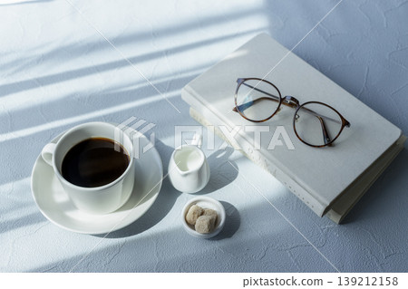 一張令人耳目一新的餐桌照片,展現了清晨閱讀和咖啡的場景,照片中擺放著眼鏡和書籍。 一張令人耳目一新的餐桌照片,展現了清晨閱讀和咖啡的場景,照片中擺放著眼鏡和書籍。 139212158