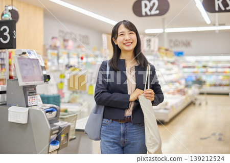 A young woman finishes paying at a self-checkout and slings her eco-bag over her shoulder. A young woman finishes paying at a self-checkout and slings her eco-bag over her shoulder. 139212524