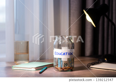 Savings jar for EDUCATION on table. Close up of money in transparent container representing financial planning and goal achievement 139212547