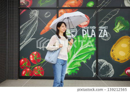 一位年輕女子撐著陽傘去超市。 一位年輕女子撐著陽傘去超市。 139212565