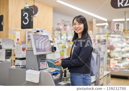 一位年輕女子正在使用智慧型手機在自助結帳櫃檯付款。 一位年輕女子正在使用智慧型手機在自助結帳櫃檯付款。 139212780