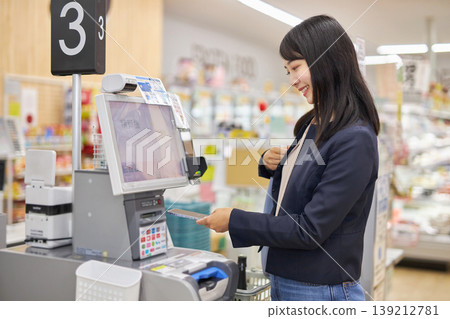 A young woman using her smartphone to pay at a self-checkout counter. A young woman using her smartphone to pay at a self-checkout counter. 139212781