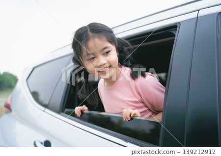 Happy girl enjoying the view from a car window with a joyful expression during a family road trip in the countryside on a sunny day Happy girl enjoying the view from a car window with a joyful expression during a family road trip in the countryside on a sunny day 139212912