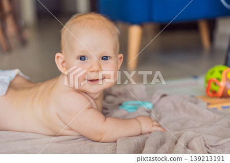 Baby lying on play mat learning to crawl and get on all fours. Infant practicing motor skills and development at home. Early childhood growth, milestones and active learning concept Baby lying on play mat learning to crawl and get on all fours. Infant practicing motor skills and development at home. Early childhood growth, milestones and active learning concept 139213191