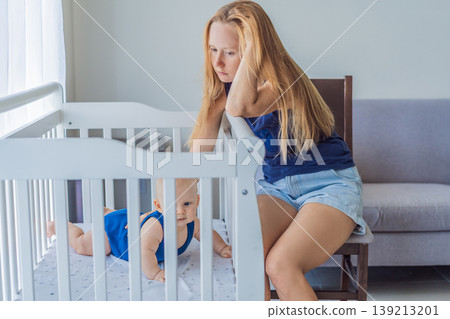 Very tired mother sitting by baby crib at home feeling exhausted. Sleep deprived mom caring for newborn at night. Parenting fatigue, motherhood stress, childcare and real family life concept Very tired mother sitting by baby crib at home feeling exhausted. Sleep deprived mom caring for newborn at night. Parenting fatigue, motherhood stress, childcare and real family life concept 139213201