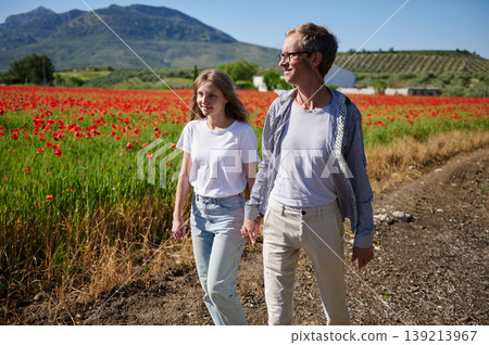 Couple Walking Hand in Hand Through Poppy Field Near Mountains On a Sunny Summer Day Couple Walking Hand in Hand Through Poppy Field Near Mountains On a Sunny Summer Day 139213967
