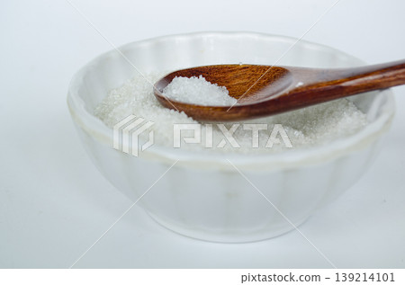 Side view of salt in wooden spoon inside white bowl highlighting seasoning ingredient and controlled sodium consumption. Side view of salt in wooden spoon inside white bowl highlighting seasoning ingredient and controlled sodium consumption. 139214101