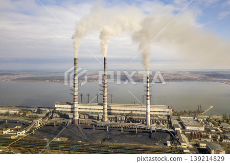 Tall pipes of power plant, white smoke on rural landscape, lake water and blue sky copy space background. 139214829