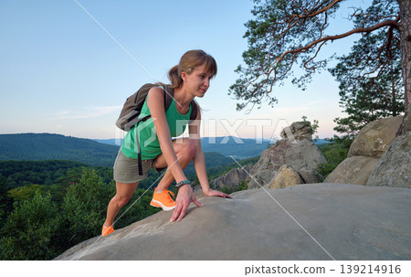Sportive woman climbing alone on hillside rocky trail. Female hiker overcoming difficult cliff on wilderness path. Active lifestyle concept 139214916