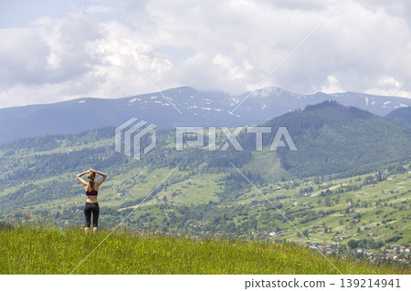 Slim young woman with raised arms outdoors on background of beautiful mountain landscape on sunny summer day. Slim young woman with raised arms outdoors on background of beautiful mountain landscape on sunny summer day. 139214941