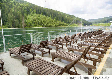 Row of empty wooden beach chairs near water. 139215013