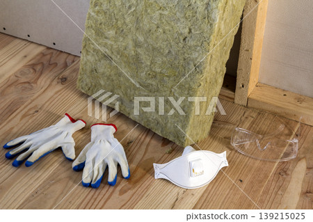Rock wool and fiberglass insulation staff material for cold barrier. Tools for work with glass wool: protective goggles, glasses and mask. Warm home, economy, construction and renovation concept. Rock wool and fiberglass insulation staff material for cold barrier. Tools for work with glass wool: protective goggles, glasses and mask. Warm home, economy, construction and renovation concept. 139215025
