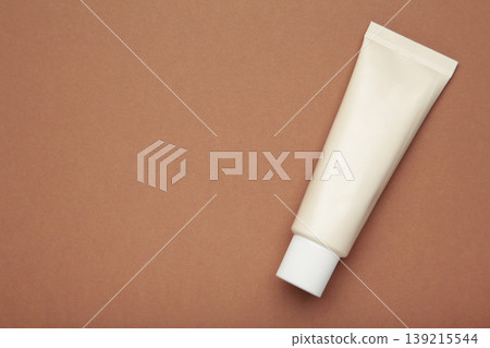 Beige tube of cream on brown background. Mockup plastic tube for cosmetics. Space for text Beige tube of cream on brown background. Mockup plastic tube for cosmetics. Space for text 139215544