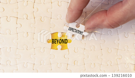Beyond expectations words symbol. Concept words Beyond expectations on beautiful white puzzles. Beautiful yellow background. Businessman hand. Business Beyond expectations words concept. Copy space. 139216010