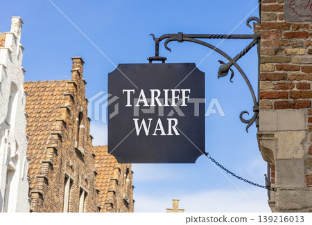 Trade tariff war symbol. Concept word Tariff war on beautiful black sign on street in Brugge. Beautiful blue sky and buildings background. Business trade tariff wars concept. Copy space. Trade tariff war symbol. Concept word Tariff war on beautiful black sign on street in Brugge. Beautiful blue sky and buildings background. Business trade tariff wars concept. Copy space. 139216013