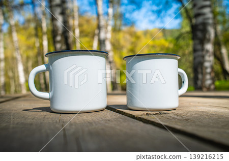 Two white enamel camping mugs on rustic wooden table with autumn birch forest Two white enamel camping mugs on rustic wooden table with autumn birch forest 139216215