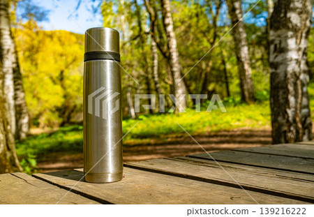 Thermos vacuum flask on wooden deck table with birch forest 139216222