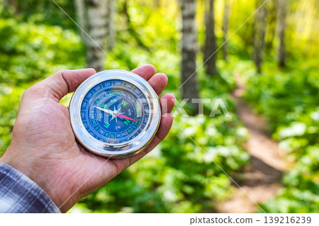 Hand holding round magnetic compass in green sunny forest, outdoor hiking navigation adventure travel Hand holding round magnetic compass in green sunny forest, outdoor hiking navigation adventure travel 139216239