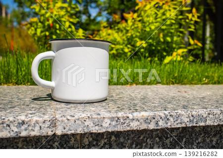 White enamel mug cup on stone ledge with green White enamel mug cup on stone ledge with green 139216282
