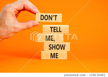 Tell or show symbol. Concept words Do not tell me, show me on beautiful wooden blocks. Beautiful orange paper background. Businessman hand. Business tell or show concept. Copy space. Tell or show symbol. Concept words Do not tell me, show me on beautiful wooden blocks. Beautiful orange paper background. Businessman hand. Business tell or show concept. Copy space. 139216401
