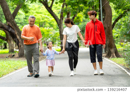 Close up Asian family with grandfather, grandchild, young mother and father hold hands and walk together along the road in public park or garden with happiness. Close up Asian family with grandfather, grandchild, young mother and father hold hands and walk together along the road in public park or garden with happiness. 139216407