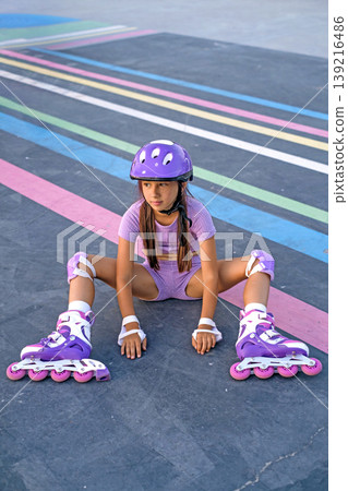 A girl with roller skates on sits on an asphalt path for skateboarding and roller skating. Sports hobbies A girl with roller skates on sits on an asphalt path for skateboarding and roller skating. Sports hobbies 139216486