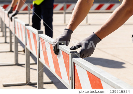 Construction workers in gloves setting up traffic barriers on a sunny day Construction workers in gloves setting up traffic barriers on a sunny day 139216824