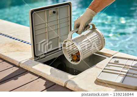 Pool maintenance worker emptying debris from a skimmer basket into the pool's filtration system Pool maintenance worker emptying debris from a skimmer basket into the pool's filtration system 139216844