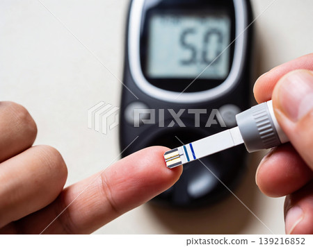 Close-up of a person using a glucose meter to check blood sugar levels on their fingertip 139216852