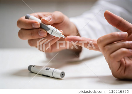 Close-up of a person using a lancet device to prick their finger for blood glucose testing Close-up of a person using a lancet device to prick their finger for blood glucose testing 139216855