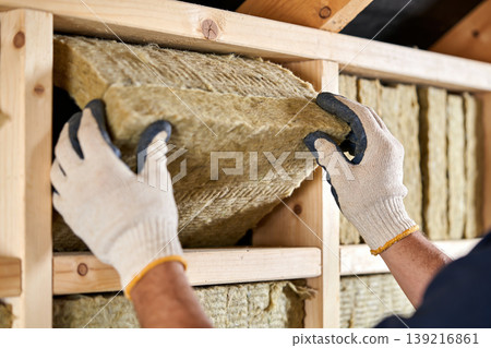 Construction worker installing thermal insulation material into wooden wall frame Construction worker installing thermal insulation material into wooden wall frame 139216861