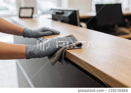 Hands wearing gray gloves wiping down a wooden reception desk with a cloth Hands wearing gray gloves wiping down a wooden reception desk with a cloth 139216868