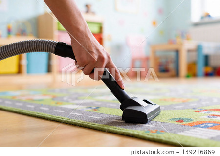 Close-up of a hand vacuuming a colorful children's rug in a bright playroom Close-up of a hand vacuuming a colorful children's rug in a bright playroom 139216869